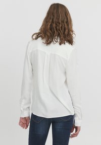 Hvid langærmet bluse med rygslidsdetalje, blødt stof og knapmanchetter, parret med mørk denim jeans.