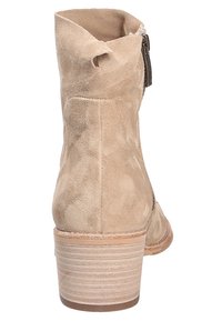 Stivaletto in suede beige con un design morbido, un tacco impilato e dettaglio con zip laterale. Texture liscia con lievi variazioni nel motivo.