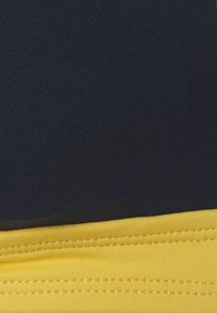 Duas secções de tecido: a parte de cima é azul-escuro com uma textura suave, e a parte de baixo é amarela brilhante com detalhes em canais e costura visível.