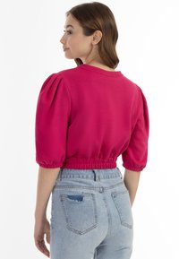 Fuchsiový krátký top s nabíranými rukávy, elastickým pasem a kulatým výstřihem, kombinovaný se světle modrými džíny s vysokým pasem.