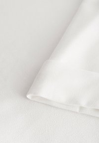 Vitt texturerat tyg med en slät yta, med en vikt kant. Ytan är jämn och subtilt mönstrad.