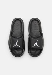 Juodi šlepetės su tekstūruotais guminiais padais, turinčios matinį paviršių, plačią dirželį ir baltą Jumpman logotipą ant kiekvienos šlepetės.