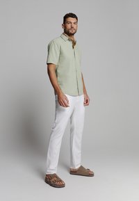 Lichtgroen short-sleeve shirt, witte linnen broek en bruine sandalen met twee banden. Gladde textuur, casual pasvorm, minimale details.