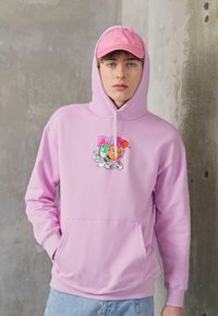 Gaiši rozā kapuce ar priekšējo kabatu un kapucīti ar aukliņu; ar krāsainu grafisko dizainu. Apvienota ar atbilstošu rozā beisbola cepuri.