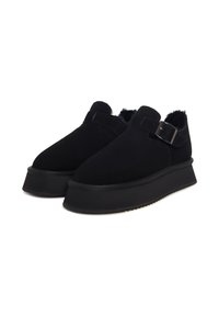 Černé semišové slip-on boty s tlustou černou platformou, vybavené bočním přezkou a měkkou kožešinovou podšívkou kolem kotníku.