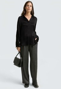 Black silk blouse with a collared neckline paired with high-waisted, textured gray wide-leg trousers. Model holds a black handbag.