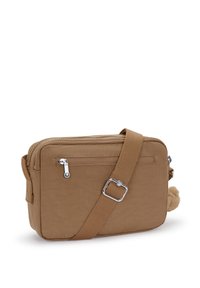 Brun stof crossbody taske med lynlåslukning, justerbar rem og en blød pom-pom detalje på siden. Firkantet form med en tekstureret overflade.