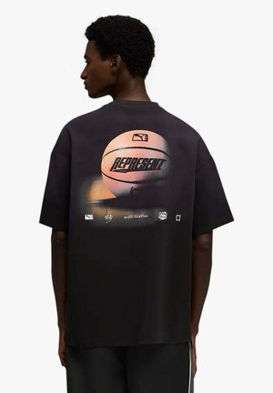 Persona che indossa una maglietta nera oversize con una grafica di un pallone da basket e la parola "REPRESENT" sul retro.