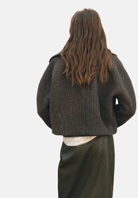 Afgekorte geruite jas in donkere tinten, met een structuurstof en brede mouwen, gecombineerd met een soepel leren rok.