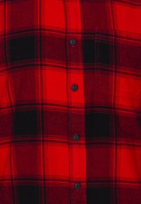 Rood en zwart geruite flanellen shirt met zwarte knopen, een borstzak en een zachte textuur met prominente horizontale en verticale lijnen.