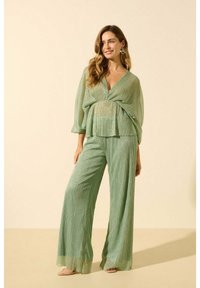 Ensemble deux pièces vert clair comprenant un haut lâche enveloppé avec un décolleté en V et un pantalon à jambes larges, tous deux avec un léger éclat et un tissu texturé.