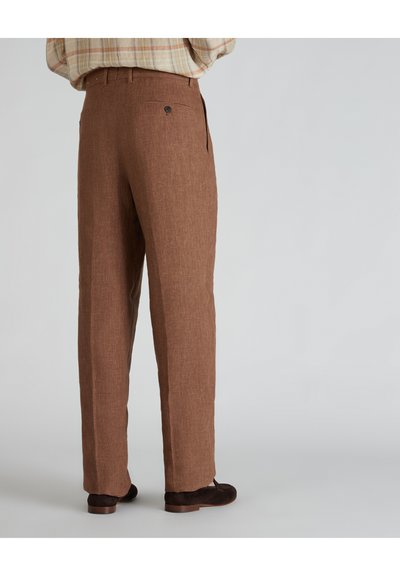 Pantaloni in lino marroni con finitura strutturata, dotati di una tasca posteriore con chiusura a bottone. Abbinati a calzature marroni scure.