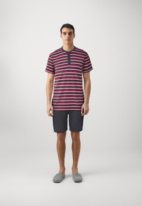 Striped short-sleeve shirt in red and navy, featuring a buttoned collar, paired with dark shorts and gray slip-on slippers.