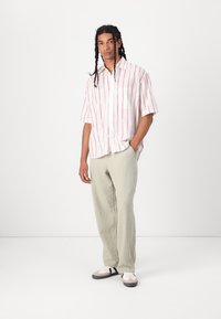 Short-sleeve button-up shirt with white and red vertical stripes. Light green, loose-fitting pants. Casual sneakers with a white and gray design.