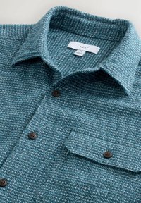 Blå tekstureret skjorte med knapper, brystlomme, mørke knapper og mellemstørrelse etikette syet indeni kraven.