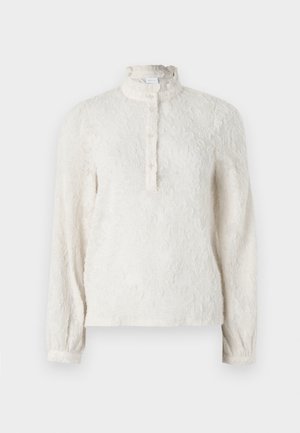 Blusa branca de manga longa com uma superfície texturizada, colarinho com volantes e frente com botões. Apresenta um padrão floral discreto por toda a peça.