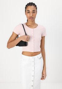 Top corto rosa a coste con maniche corte e chiusura anteriore a bottoni. Abbinato a una gonna di jeans bianca con bottoni argentati e una borsa nera.