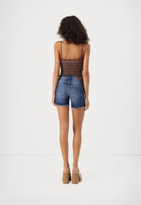 Un débardeur marron à smocks associé à un short en denim bleu clair, avec un ourlet effiloché et des poches arrière. Des sandales à talons beiges complètent le look.