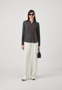 Košulja s dugim rukavima na dugme s multikolor geometrijskim uzorkom, uparenih s širokim bijelim hlačama i crnom torbom. Glatka tekstura tkanine.