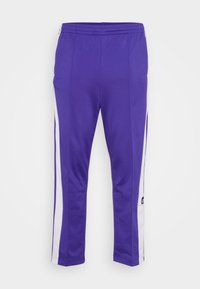 Fialové sportovní kalhoty vyrobené z elastického materiálu s bílými bočními pruhy a elastickým pasem. Na levé nohavici se nachází logo.
