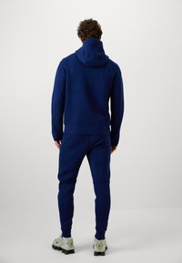 Marineblå hættetrøje og matchende joggers lavet af blødt materiale, med en afslappet pasform og ribbede manchetter. Indeholder en stor hætte og ensartet design.