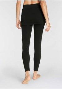 Zwarte leggings met een aansluitend ontwerp en een middellange rokoverlay. De stof lijkt glad en rekbaar, geschikt voor actieve kleding.