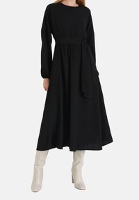 Mustat, pitkät hihat, tiukka vyötärö ja valuva hame; siinä on vyösolki ja pehmeä kangas, yhdistettynä valkoisiin polviin ulottuviin saappaisiin.