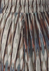 Bloemmotiefstof in tinten bruin, blauw en crème, met een elastische tailleband en verticale strepen voor textuur.