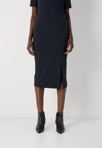 Navy fitted midi skirt with a side slit, crafted from stretchy fabric. Paired with black ankle boots for a sleek look.