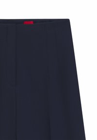 Navy blue tailored trousers with a flat-front design, featuring sharp creases and a contrasting red tag at the waistband.