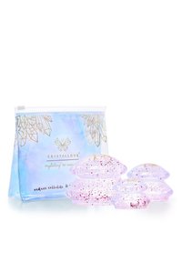 Zestaw trzech przezroczystych, różowawych kubków do ciała z brokatowymi akcentami, zapakowanych w jasnoniebieską saszetkę z złotym geometrycznym wzorem.