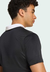 Schwarzes Sportshirt mit weißem Kragen, kurzen Ärmeln und strukturiertem Stoff. Das Design legt Wert auf Atmungsaktivität und Komfort.