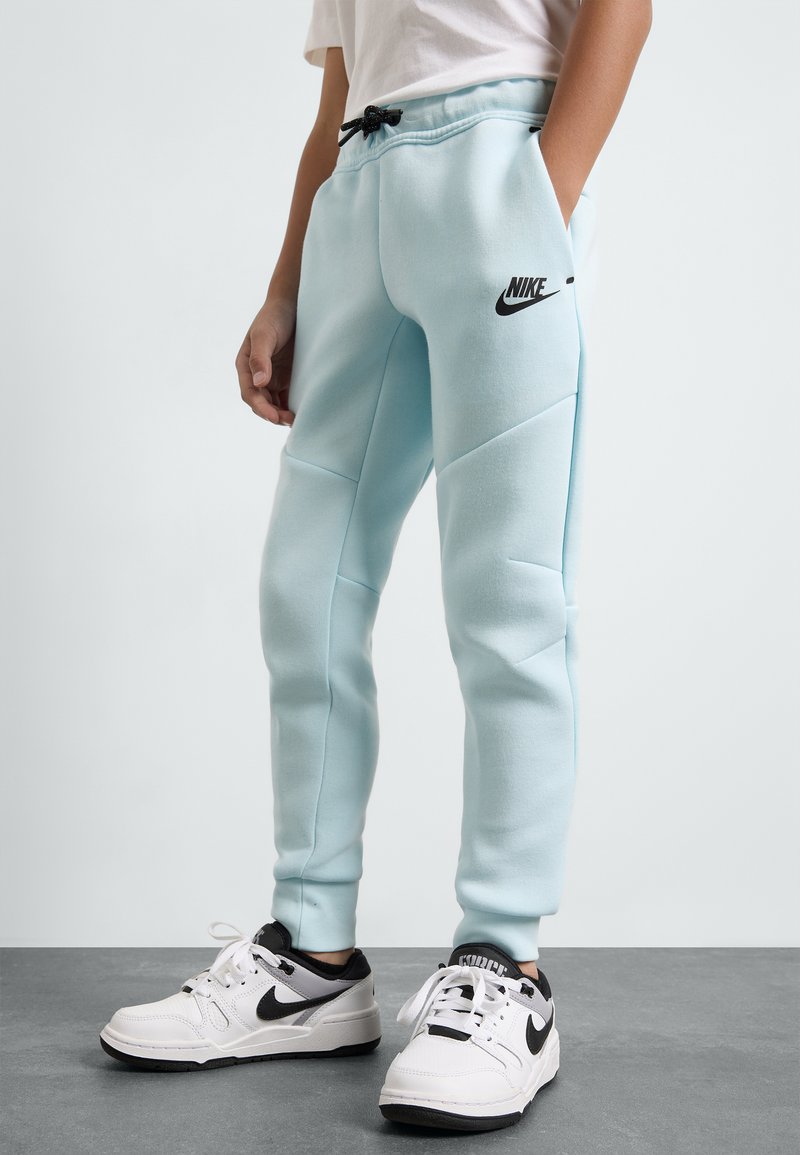 Šviesiai mėlynos, siauro kirpimo Nike sportinės kelnės su juodu logotipu. Yra elastinė juosmens juosta su raišteliu ir šoninės kišenės. Nešiojamos su baltomis sportbačiais.