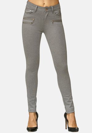 Jeans ajustados grises con bolsillos con cremallera, diseño elegante y textura suave. Combinados con tacones altos negros para un aspecto moderno.
