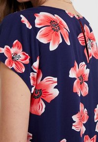 Námořnické šaty s velkými růžovými květinovými vzory, krátkými rukávy a malým detailním klíčovým otvorem na zadní straně. Vyrobeno z lehkého materiálu.