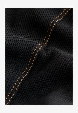 Nærbillede af sort ribbet stof med to parallelle rækker af gulbrune sting på en let kurve.