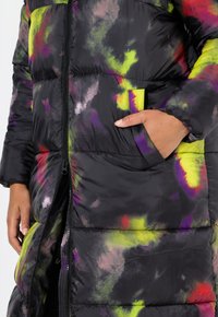 Piumino nero con vivaci spruzzi di verde, viola e rosso. Include una zip frontale e tasche laterali con accenti elastici.