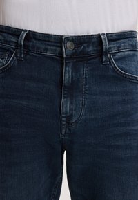 Jeans en denim bleu foncé avec une coupe classique, dotés d'une fermeture à bouton, d'un design à cinq poches et d'un léger délavage autour des cuisses.