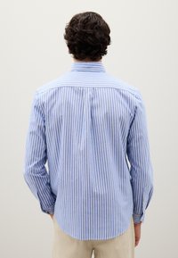 Camisa de manga larga a rayas azules y blancas con cuello abotonado, yugo visible y detalles en los puños. Ajuste entallado con dobladillo curvado.