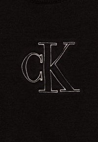 Czarny sweter z materiału o teksturowanym splocie. Posiada duże, białe haftowane logo "CK" na środku.