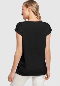 Black short-sleeve t-shirt with rolled sleeves and a relaxed fit. Soft, smooth fabric. Back view shows curved hemline and simple design.