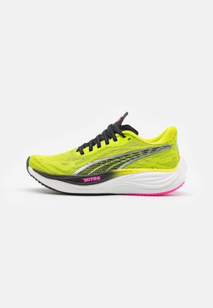 Zapatilla de correr de color amarillo brillante con parte superior de malla transpirable, acentos en negro y plata, entresuela blanca acolchada y detalle de suela rosa.