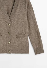 Ruskea neulottu villatakki, jossa on neljä metallipainiketta, kaksi etutaskua, ribbaus hihansuissa ja helmoissa, esitetty tasaisena valkoisella taustalla.