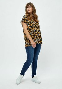 Sort floral bluse med korte ærmer, prydet med orange blomster, parret med mørkeblå skinny jeans og hvide sneakers.