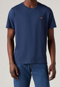 Námořnická modrá bavlněná tričko s kulatým výstřihem a krátkými rukávy; má malé červené logo Levi's na levé straně hrudi.