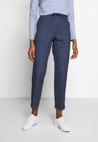 Pantalon jogger bleu marine ajusté avec une taille à cordon, poches latérales et ourlets retroussés, confectionné dans un tissu texturé. Associé à des baskets blanches.