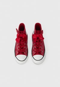 Ténis altos vermelhos com bicos de borracha branca, acabamento de sola preta e laços de cetim vermelhos nos atacadores, exibidos de cima sobre um fundo branco.