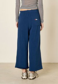 Pantalons larges marine en tissu doux, dotés d'une poche arrière avec broderies colorées. L'ourlet est légèrement arrondi en bas.