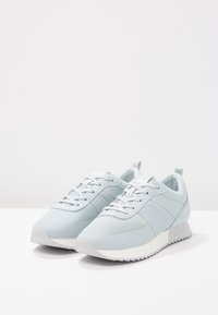 Baskets bleu clair avec dessus en mesh et synthétique, lacets plats et semelle en caoutchouc texturée. Présentent des rayures discrètes et une languette au talon.