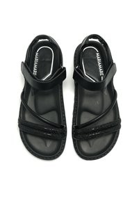 Sandalias planas negras con correas texturizadas, que presentan una correa en el tobillo trasero y una suela de goma lisa. Diseño simple con un mínimo de detalles.